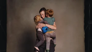A tall person is holding two small humans in their arms