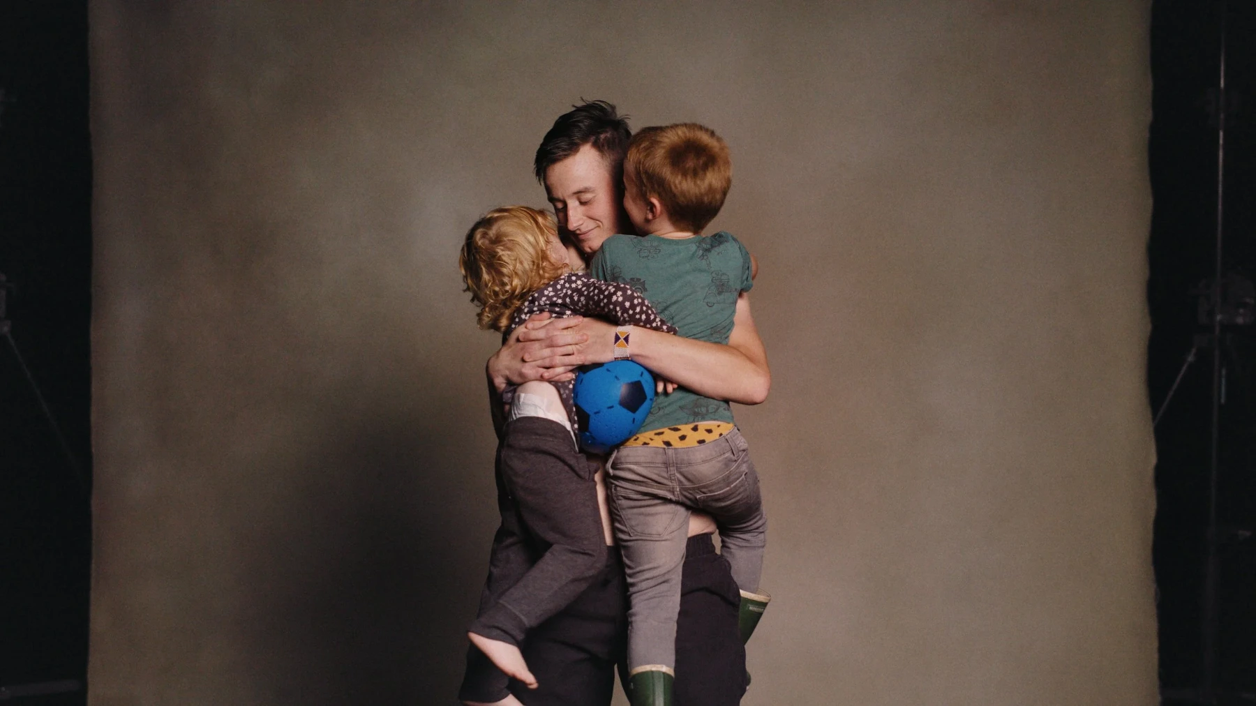 A tall person is holding two small humans in their arms