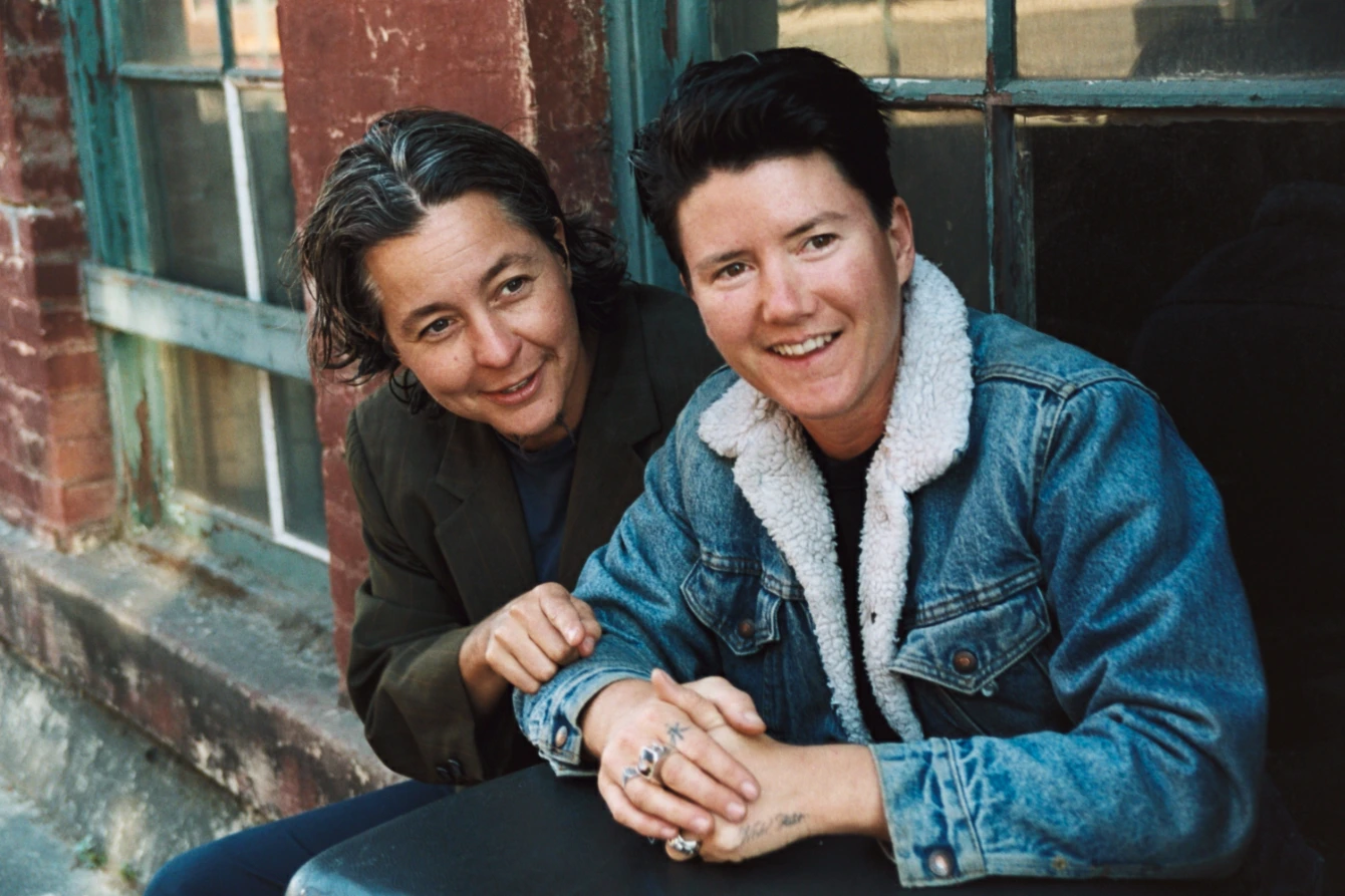 Two people are sitting next to each other in front of a window.
