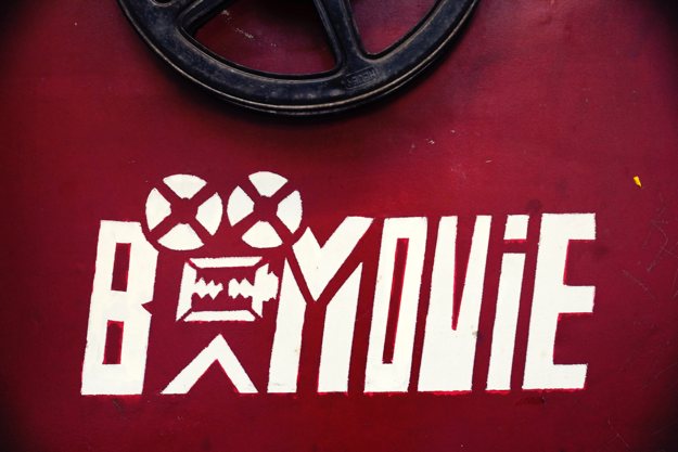 Weißes B-Movie Logo auf dunkelrotem Hintergrund.