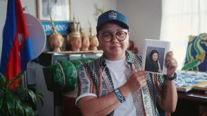 Person mit Baseball Cap hält ein Foto hoch.